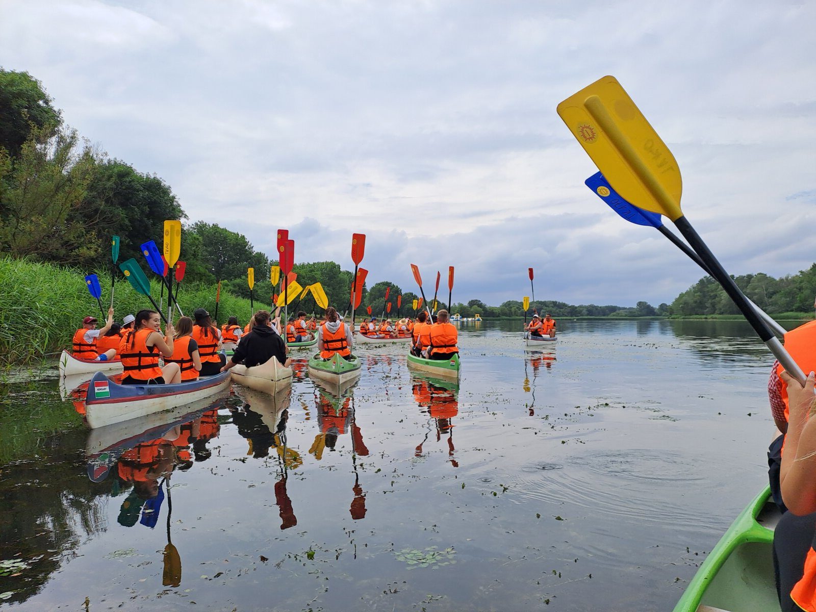 Céges csapat kenukban a Tisza-tavon, az evezők a magasban